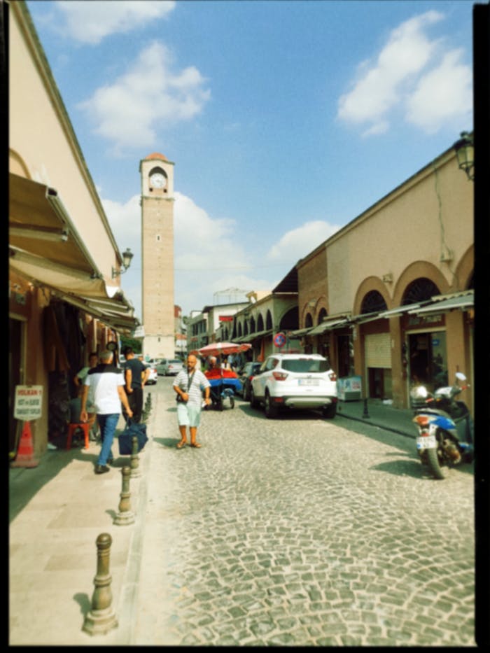 Charming cobblestone street with clock tower and vibrant urban life under sunny skies.
