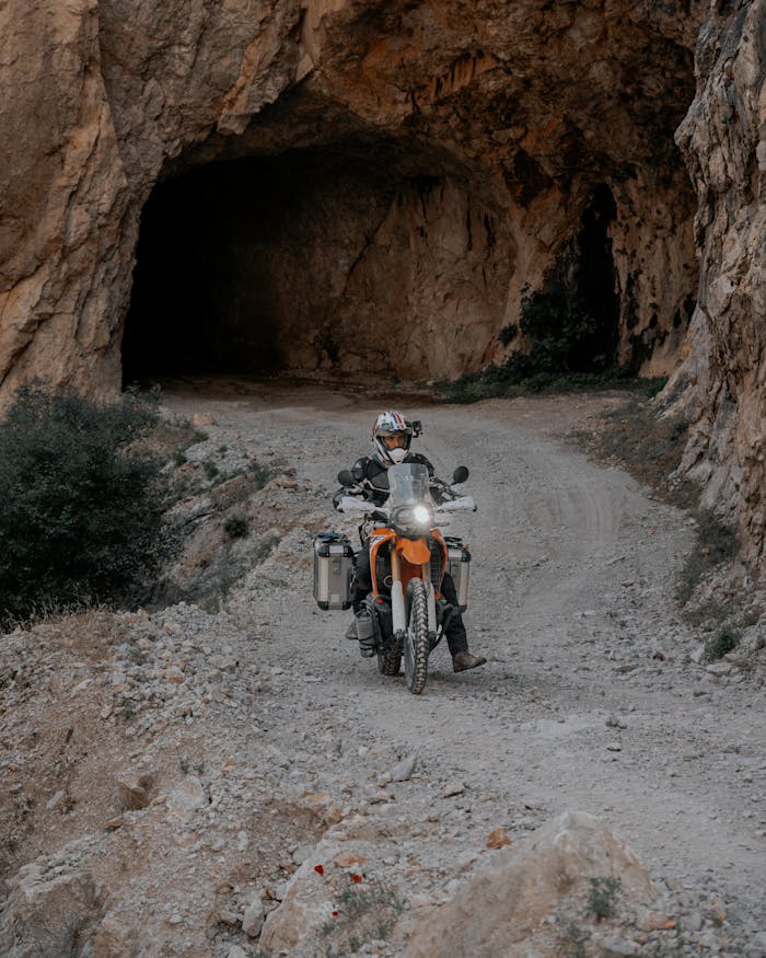 Motorcyclist navigating a rugged dirt road through a rocky tunnel. Perfect for adventure themes.