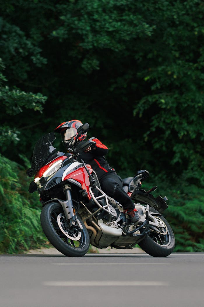 Motorcyclist wearing helmet rides on a red motorcycle along a forested road, showcasing dynamic motion.
