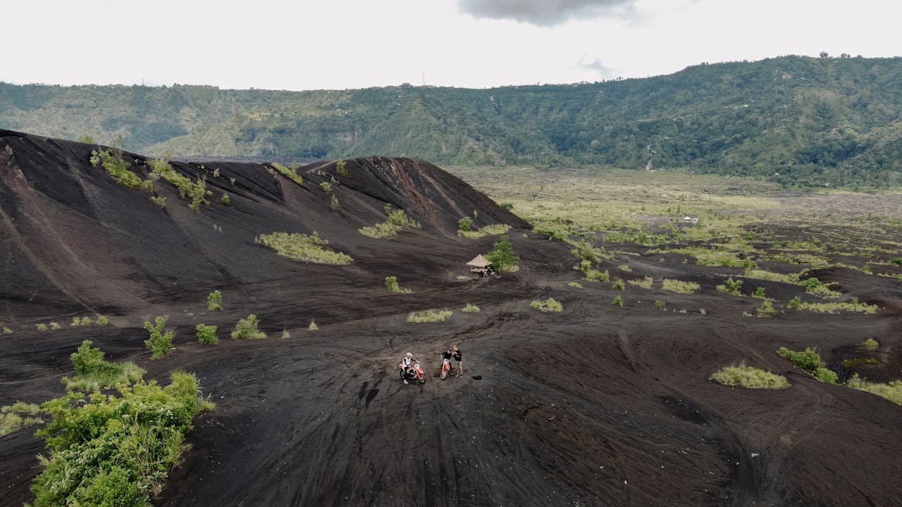 Riders on motorcycles explore a rugged volcanic landscape, surrounded by lush greenery.